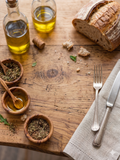 Wooden table with bread, olive oil, herbs, and cutlery on a rustic setting